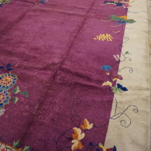 Deep purple rug with a cream border features multicolor elaborate floral designs on wood flooring.