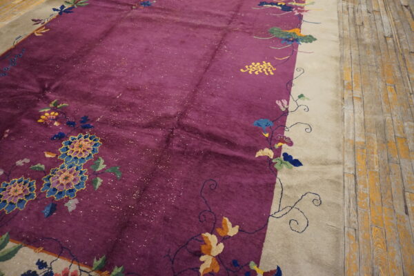Deep purple rug with a cream border features multicolor elaborate floral designs on wood flooring.