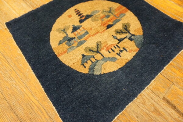 Dark blue rug square featuring a circular gold, blue, and green landscape medallion on wood floor planks.