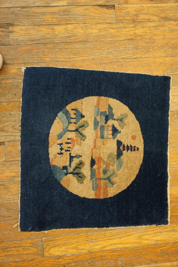 Square navy rug with a circular tan medallion featuring stylized blue, green, and orange patterns on hardwood flooring.