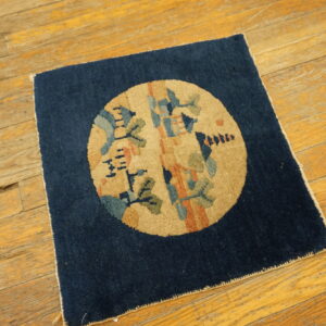 Square navy rug with a tan medallion and abstract green and blue patterns on distressed wood flooring.