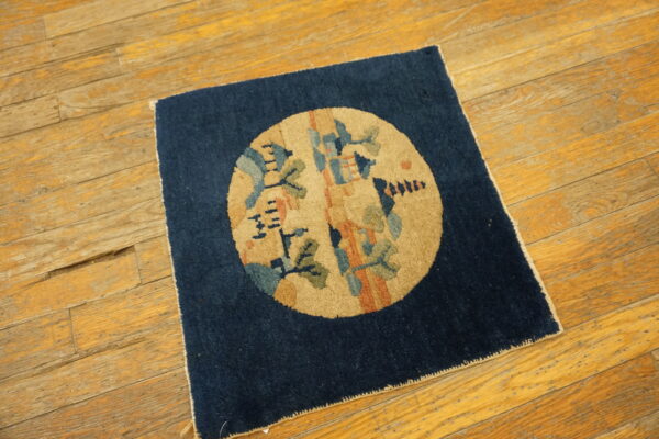 Square navy rug with a tan medallion and abstract green and blue patterns on distressed wood flooring.
