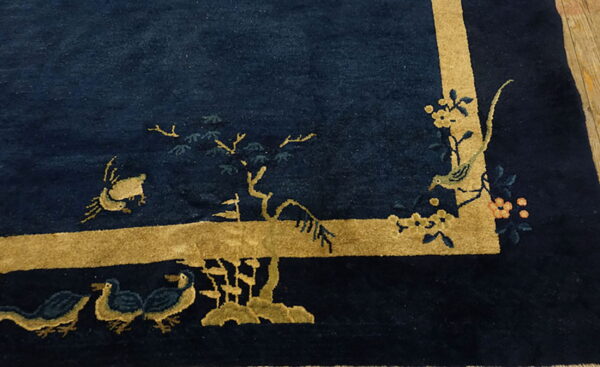 Textured dark blue rug featuring a wide gold border and stylized scenic motifs of birds and branches.