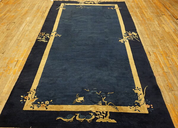 Navy blue rug on a plank wood floor has a golden border and stylized bird and floral motifs.