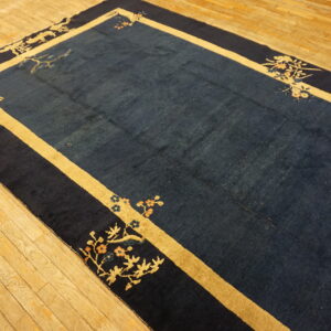 Navy blue rug with wide gold borders and floral corner designs lying on a light wood floor.
