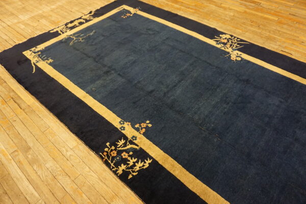 Navy blue rug with wide gold borders and floral corner designs lying on a light wood floor.