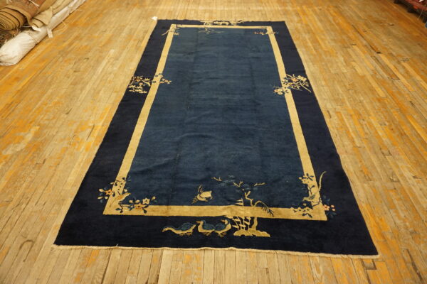 Navy blue rectangular rug with beige borders and bird motifs lies on distressed golden wood planks.