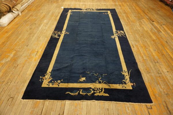 Plush navy blue rug featuring tan borders and corner botanical designs on wide wooden planks.