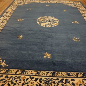 Slate blue rug with cream, gold, and dark blue floral border designs on wooden plank flooring.