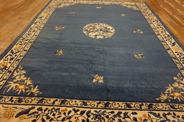 Slate blue rug with cream, gold, and dark blue floral border designs on wooden plank flooring.