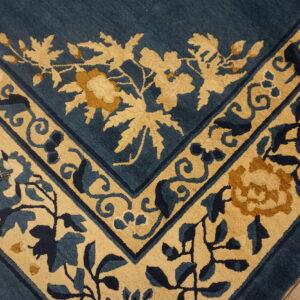 Blue and tan high-pile rug border with elaborate floral motifs shown on rustic wood planks.