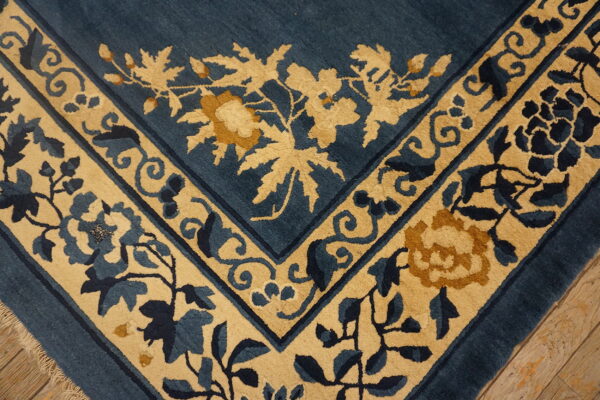 Blue and tan high-pile rug border with elaborate floral motifs shown on rustic wood planks.