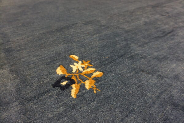 Blue area rug features a detailed floral pattern in gold, creamy white, and navy.