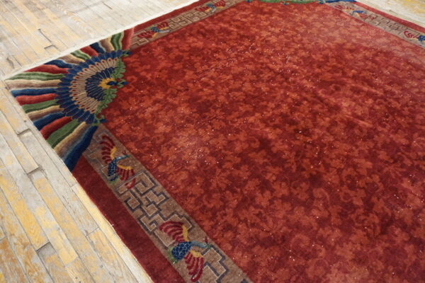 Red faded rug with a tonal field and a vibrant corner border featuring blue, green, and red fan designs.