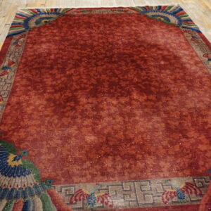 Low pile reddish-orange rug featuring a subtle floral field and colorful stylized blue and green corner patterns.