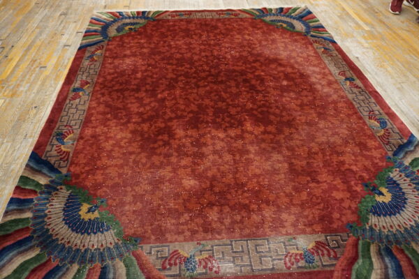 Low pile reddish-orange rug featuring a subtle floral field and colorful stylized blue and green corner patterns.