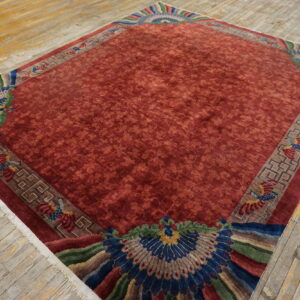 Red floral rug with brown geometric borders and large, colorful peacock motifs on weathered wood floor.