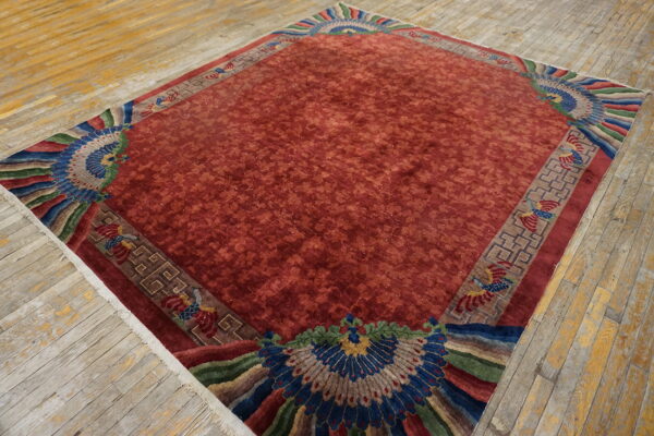Red floral rug with brown geometric borders and large, colorful peacock motifs on weathered wood floor.