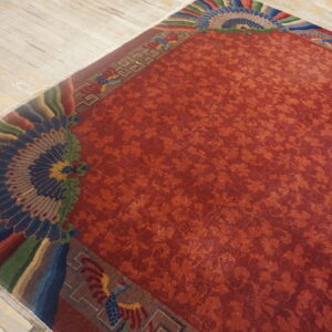 Rust-colored rug with low pile, subtle repeating patterns, and elaborate fanned borders on light wooden flooring.