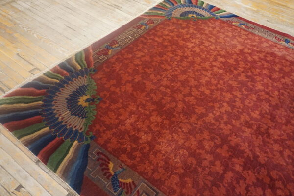 Rust-colored rug with low pile, subtle repeating patterns, and elaborate fanned borders on light wooden flooring.