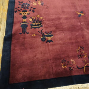 A plush red-violet rug featuring blue and gold oriental motifs rests on light, worn hardwood flooring.