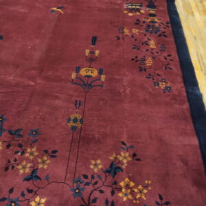 Plush red-violet rug with navy blue and yellow floral and lantern motifs on exposed wood flooring.