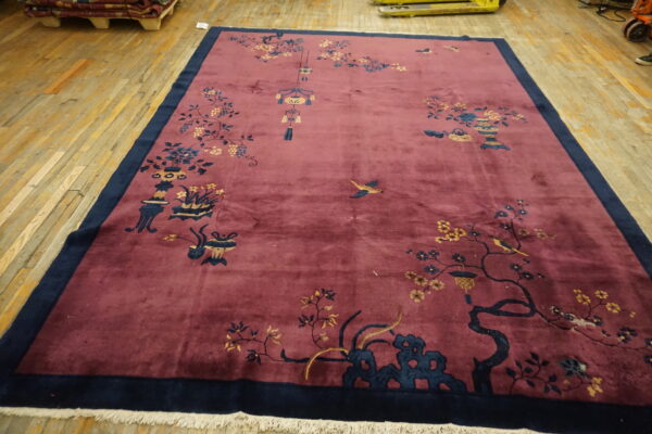 Large red rug with dark blue borders and traditional botanical patterns lies on light wooden floorboards.