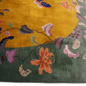 Angled view of a mustard yellow and sage green rug with large multicolored floral and vine designs.