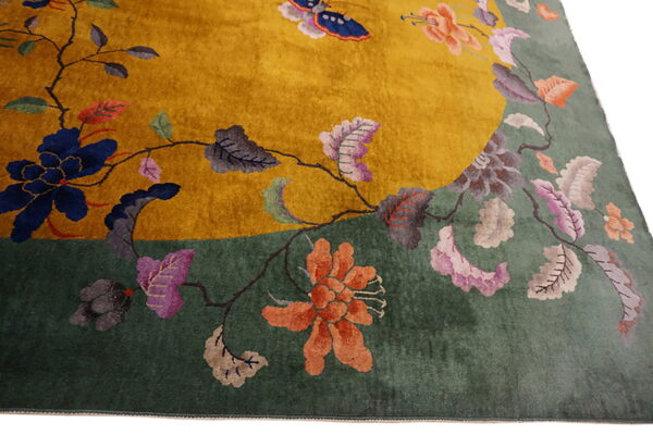 Angled view of a mustard yellow and sage green rug with large multicolored floral and vine designs.