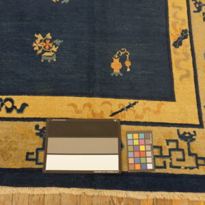 Navy blue rug with a gold border and patterned motifs, showing fringe, on wood floor with color charts.