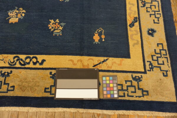 Navy blue rug with a gold border and patterned motifs, showing fringe, on wood floor with color charts.