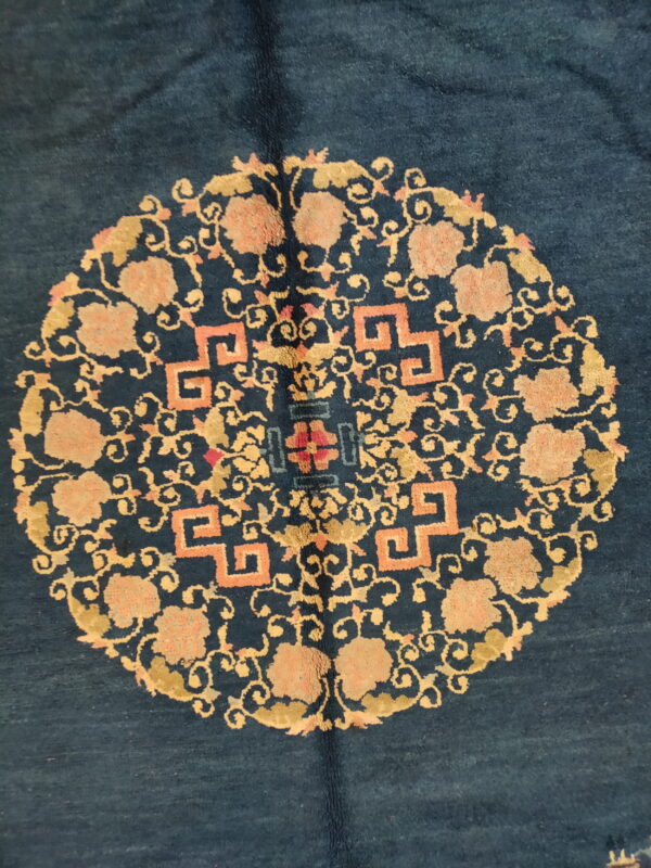 Dark blue rug with a centralized gold and peach medallion featuring geometric fretwork and floral designs.