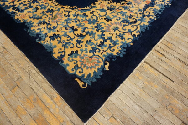 A dark blue border and gold scrolling floral rug corner rests on aged, light brown wooden floorboards.