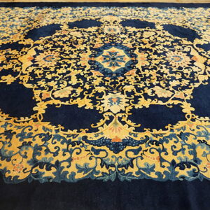 A navy and gold Oriental-style rug with intricate floral motifs rests on light wood planks.