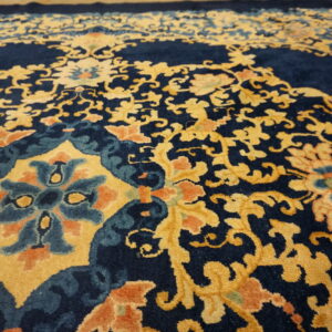 Close-up of a rug featuring a detailed floral and vine pattern in navy blue, golden yellow, teal, and orange.