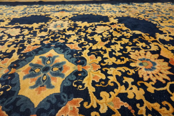 Close-up of a rug featuring a detailed floral and vine pattern in navy blue, golden yellow, teal, and orange.