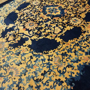 Ornate navy blue rug with gold and pale blue floral vines laid on a wood floor.