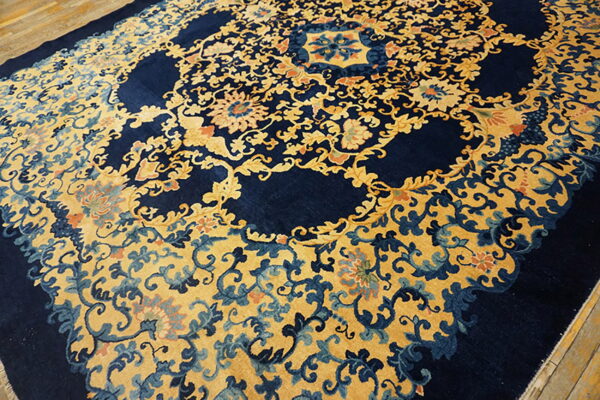 Ornate navy blue rug with gold and pale blue floral vines laid on a wood floor.