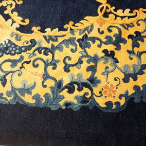 Close-up of a rug border featuring blue and gold scrolling patterns adjacent to solid navy pile.