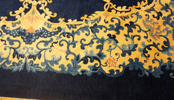 Close-up of a rug border featuring blue and gold scrolling patterns adjacent to solid navy pile.