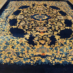 Navy blue rug with ornate golden yellow floral pattern and medallions displayed on light wood floors.