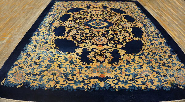Navy blue rug with ornate golden yellow floral pattern and medallions displayed on light wood floors.