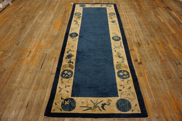 Dark blue runner rug with a wide tan border and blue symbolic motifs rests on distressed plank floor.