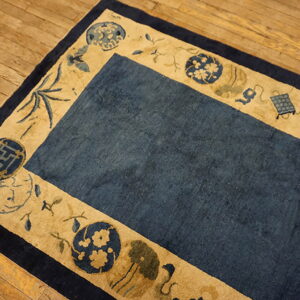 Blue and tan rug featuring geometric and floral motifs in the border, placed on wooden planks.