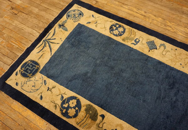 Blue and tan rug featuring geometric and floral motifs in the border, placed on wooden planks.