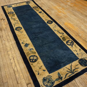 Long dark blue runner rug with tan and navy patterned borders on a distressed wood floor.