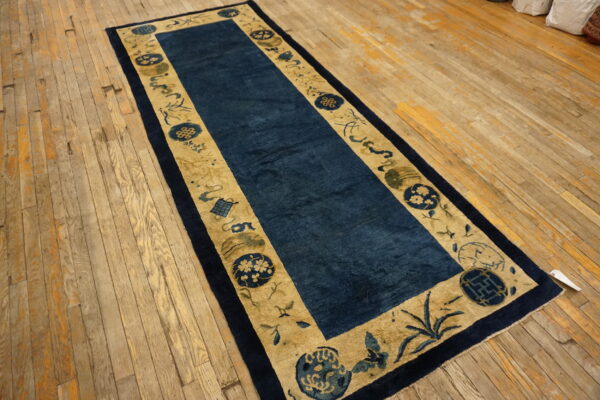 Long dark blue runner rug with tan and navy patterned borders on a distressed wood floor.
