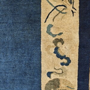 Close-up of a deep blue rug field bordering a tan stripe with stylized dark blue and green motifs.