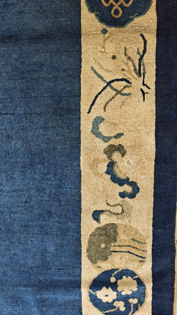 Close-up of a deep blue rug field bordering a tan stripe with stylized dark blue and green motifs.