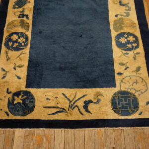 Dark blue rug with a wide tan border featuring medallions and florals on distressed wood flooring.